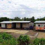 A variety of local crops laid out on black tarps. One of the typical timber houses in the back is painted with an ad for the last presidential election in Peru.