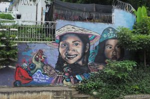 This street art piece is to the far right of the cemetery entrance. Also, look across the street: there's a large man's head painted onto the sidewall of a house!
