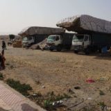 Trucks at a market, stacked really high with hay bales for sale.
