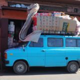 A blue Ford van, with the roof rack stacked really high.