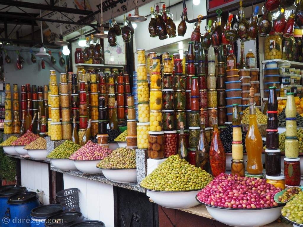 A display of pickled olives, peppers, and other vegetables in glass containers and open bowls.