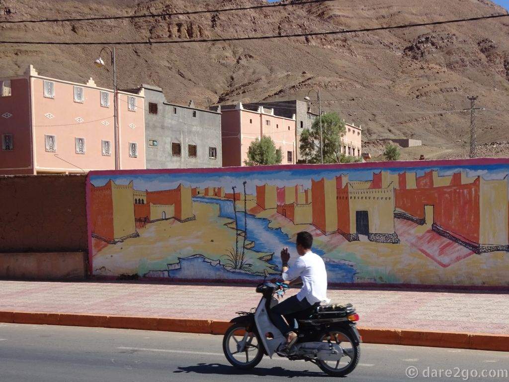 A wall painting of a traditional Berber village in front of modern apartment buildings.