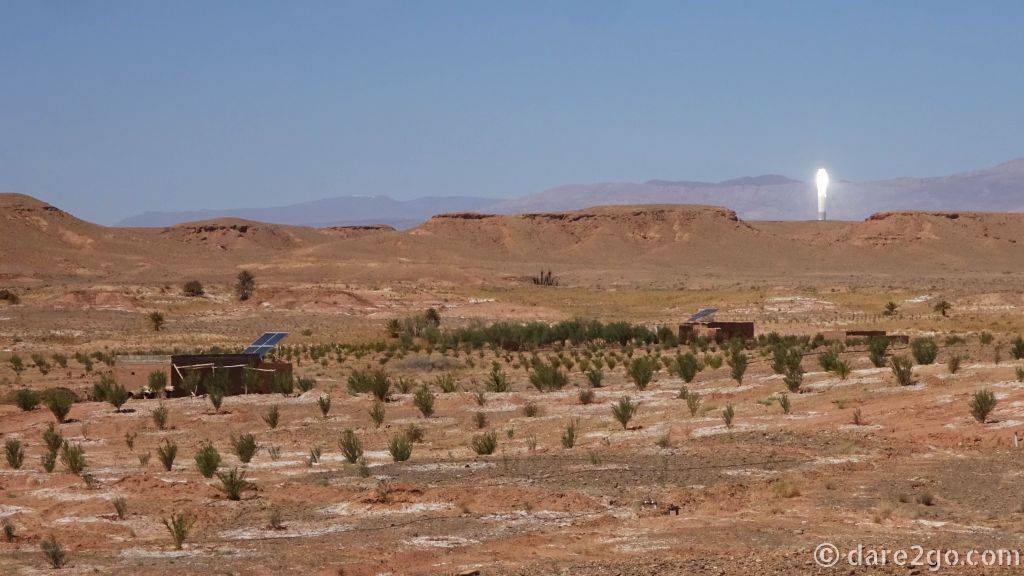 Dry desert landscape near Ouarzazate in Morocco: in the foreground 2 farms with large solar panels to power pumps, in the background the collection tower from the NOOR power plant.