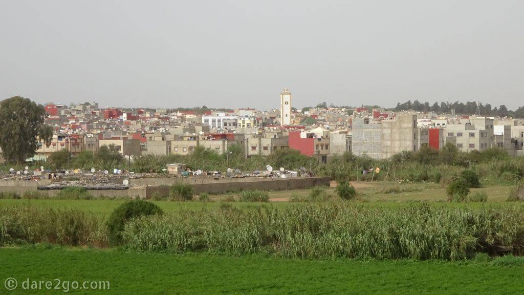 Looking across a green field to a typical town in the north of Morocco. Mostly 3 to 4 storey high residential buildings.