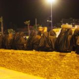 A line of women, all wrapped in black shawls, at a festival.