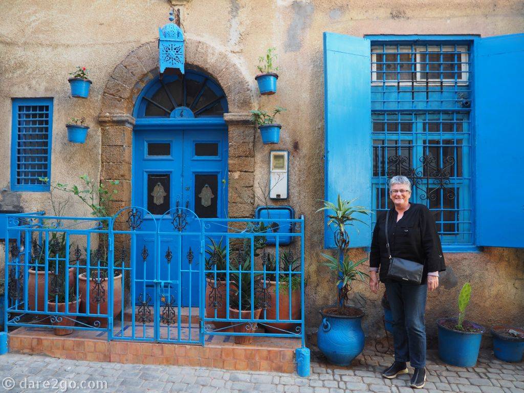 Yasha standing in front of an older house in El Jadida. All windows, doors, shutters, and flower pots are painted in a strong blue - a typical colour for Morocco.