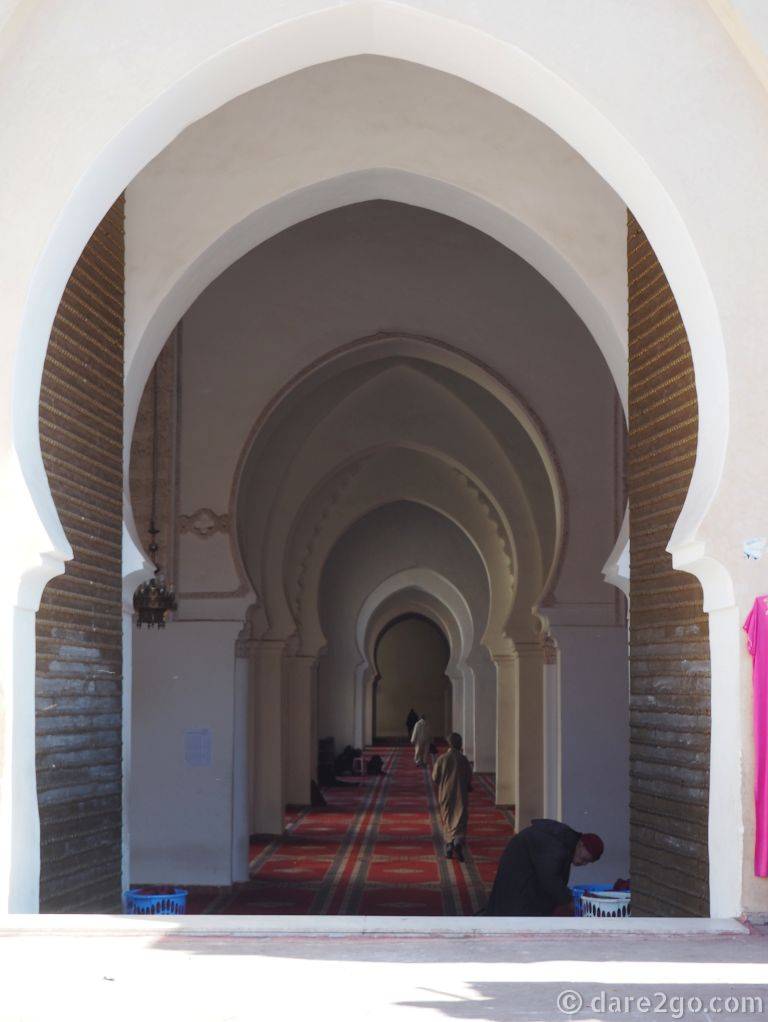 Looking through a series of horseshoe shaped archways that lead into the Kasbah Mosque of Marrakech. Some robed men making their way in for prayers.