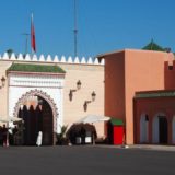 One of the gates of the Royal Palace in Marrakech. The gate is ornate but the walls are plain. Several guards and security men are present.