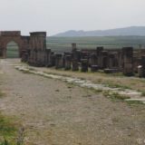 Ruins of roman houses alongside a main road heading toward the triumphal arch.