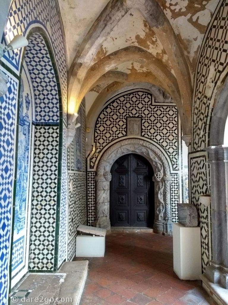 A cloister decorated with tile panels and a manueline carved stone door surround.