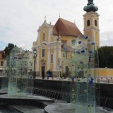A fountain of clear glass sheets, embellished with colourful glass pieces, stands at the entrance of the Vienna Gate Square into the historic centre of Győr.
