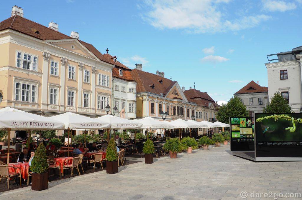 A row of famous Baroque buildings on Széchenyi Square in Győr: the pale green building with the rounded corners is the Iron Stock House, the one down from it the Apátúr House. On the far right more of the Bence Máté exhibition panels.
