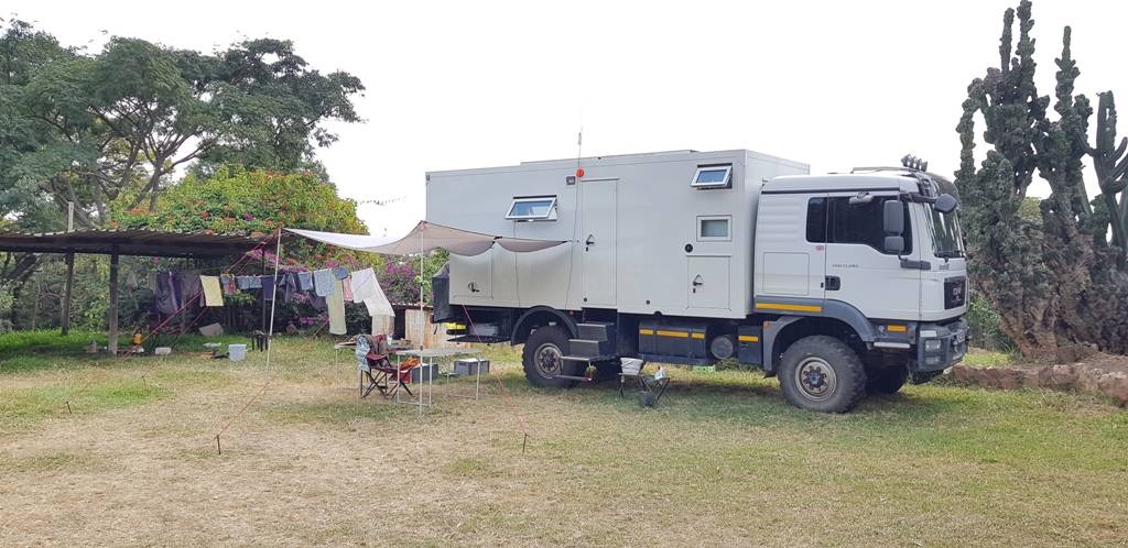 Glad to have found a nice, secure place to be under lockdown in Zambia [a large overland truck parked in a tropical garden]