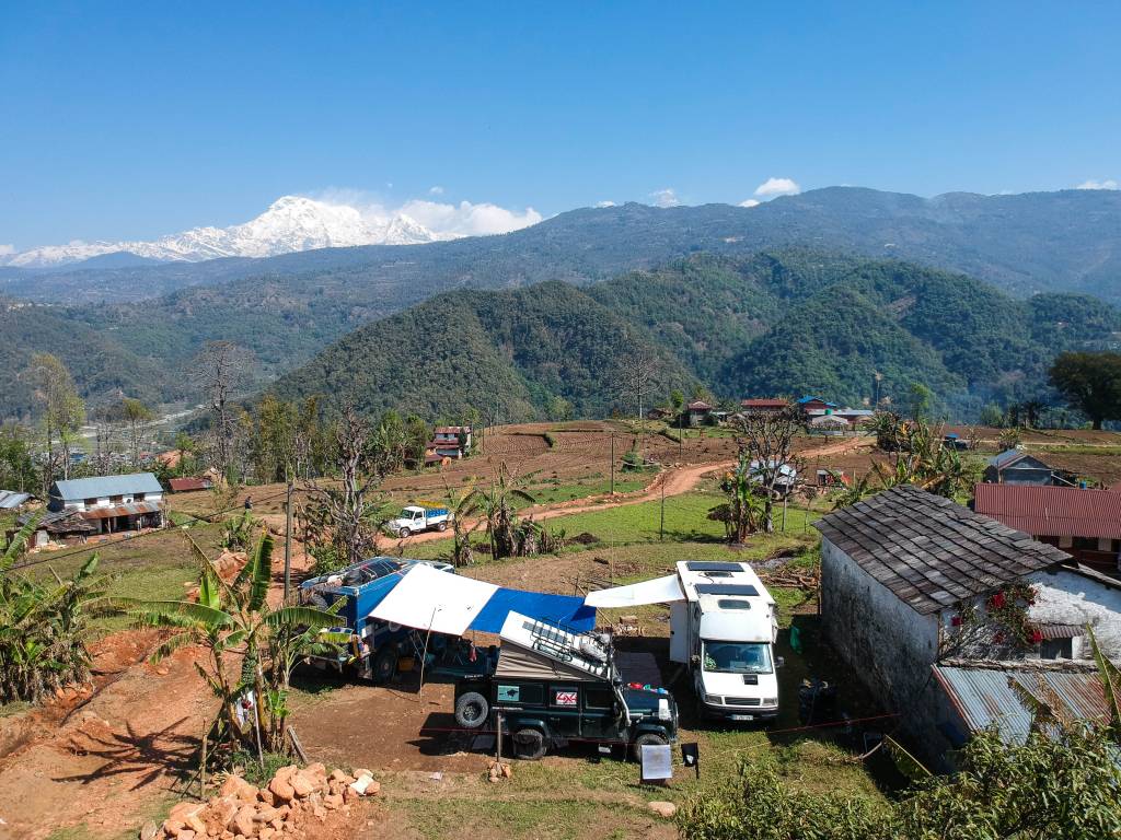 Three overland vehicles parked up in lockdown on a property in Nepal - with a vista of the magnificent Himalaya mountains
