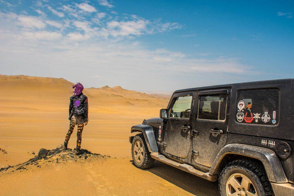 Joanie standing next to her trusty Jeep, Beauty, in a desert landscape
