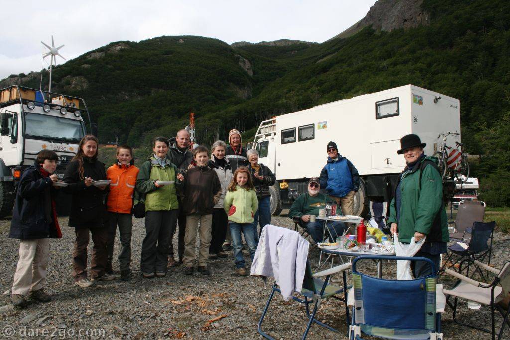 A group of overlanders gathered around a bbq, large overland vehicles in the background.