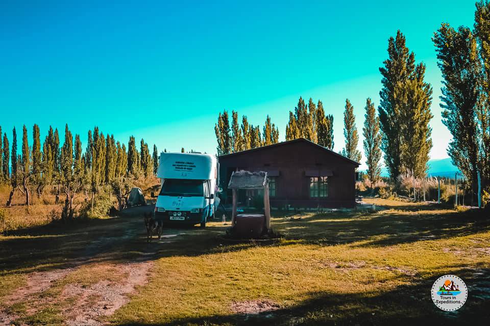 An RV pakerd outside a small wooden house
