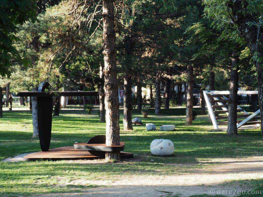 Next to the row of sculptures are more art objects placed onto the grass under the shady trees.